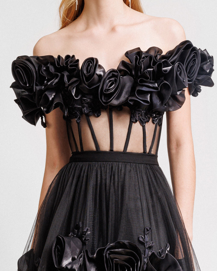 A close-up of a black evening dress with off-the-shoulders draped florals featuring a see-through corset and flared tulle skirt with floral draping.