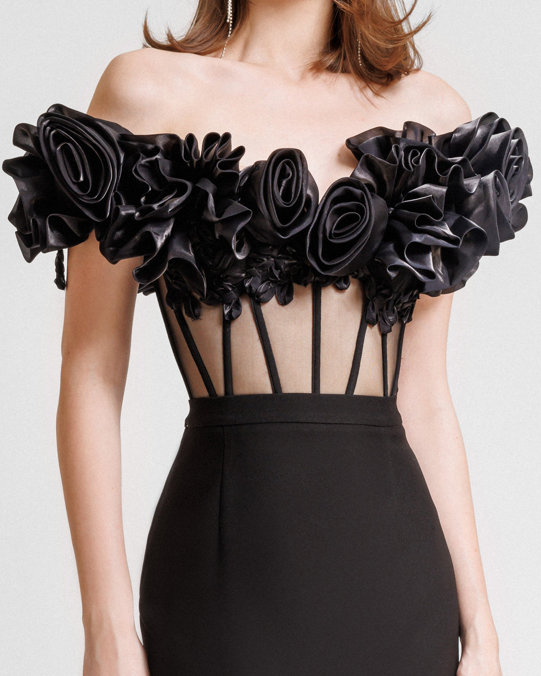 A close-up of an evening wear set featuring an off-the-shoulders draped floral black corset paired with a midi black skirt with draped florals on the hemline.