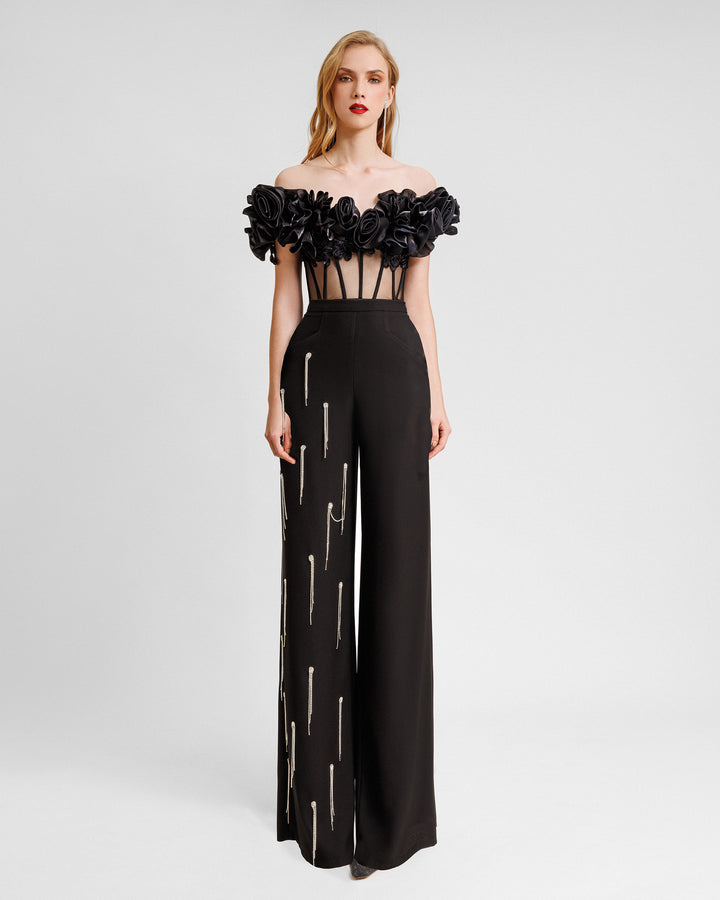 A black evening wear set featuring an off-the-shoulders draped floral corset with a see-though bodice and a straight-cut black pants with beading fringes on a single leg.