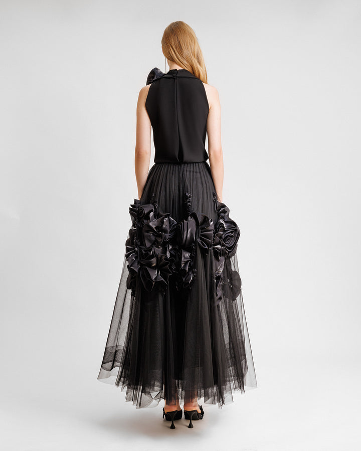 The back of a black midi dress featuring a loosely draped top adorned with floral draping on the shoulders, and a tulle skirt embellished with floral draping.