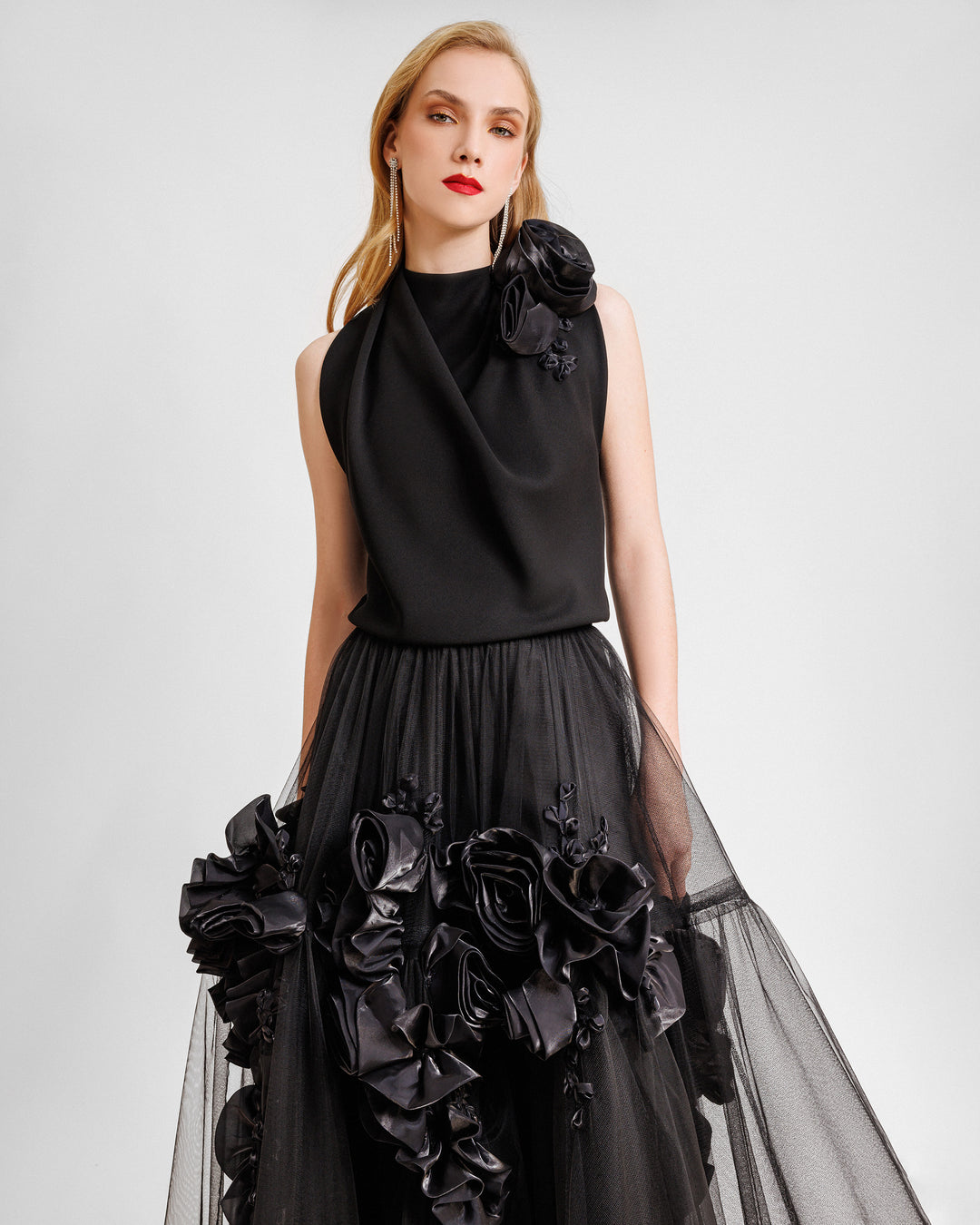 An evening wear set featuring a draped loose top with florals on the shoulder and a black tulle skirt with floral draping.