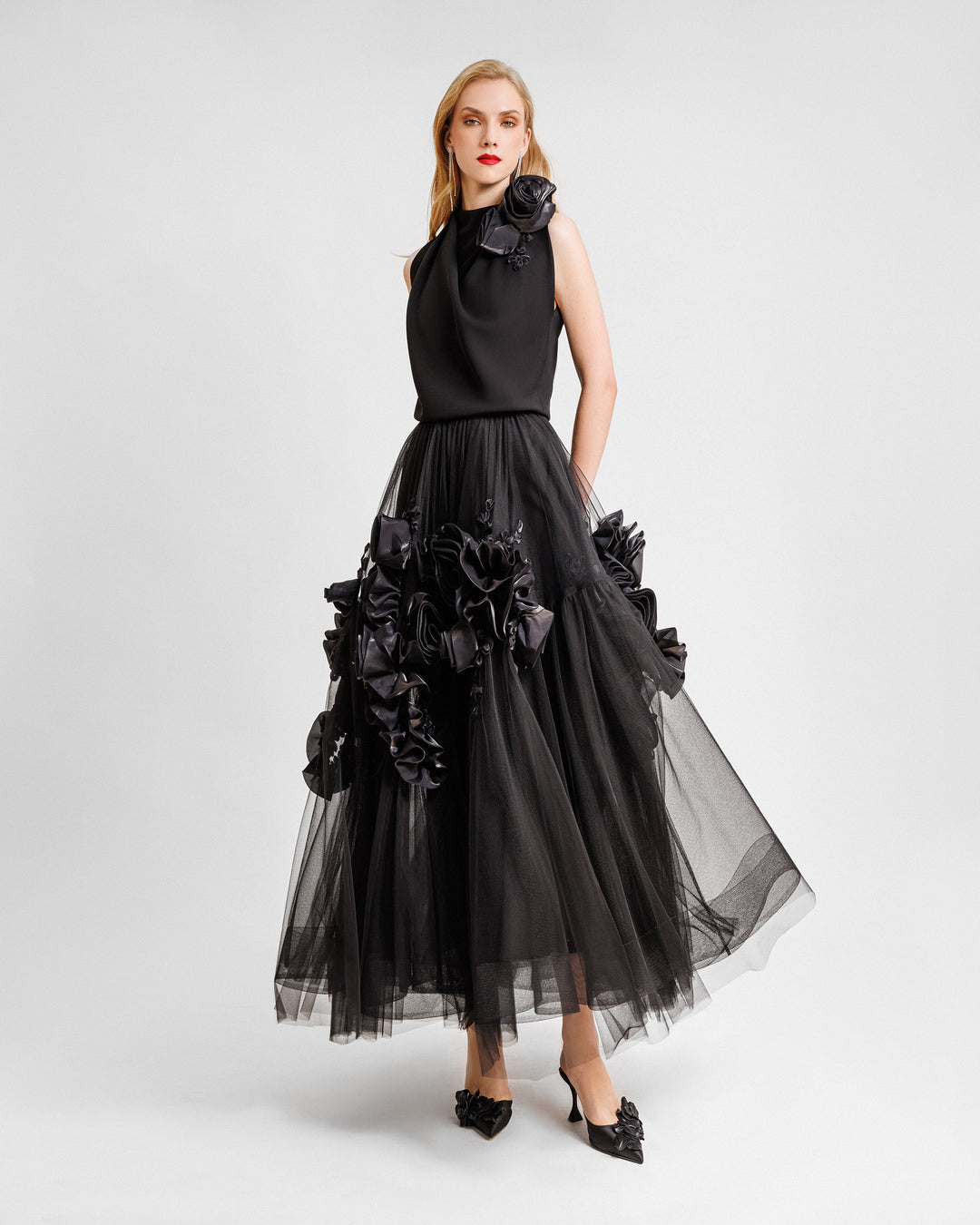 A black midi dress featuring a loosely draped top adorned with floral draping on the shoulders, and a tulle skirt embellished with floral draping.