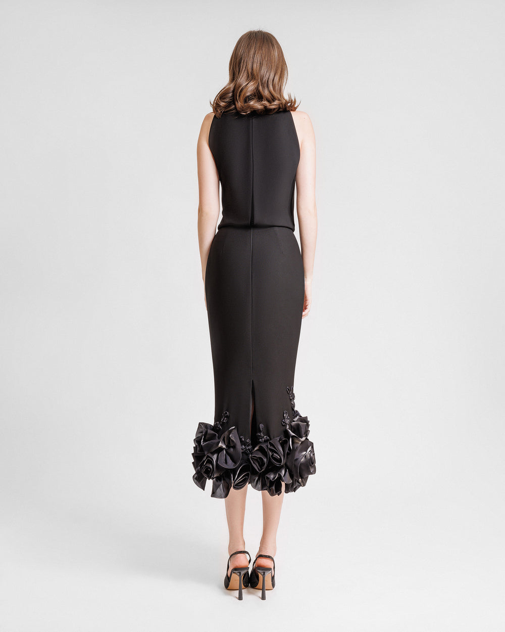 The back of an evening wear set featuring a draped loose black top paired with a midi skirt with draped florals on the hemline.