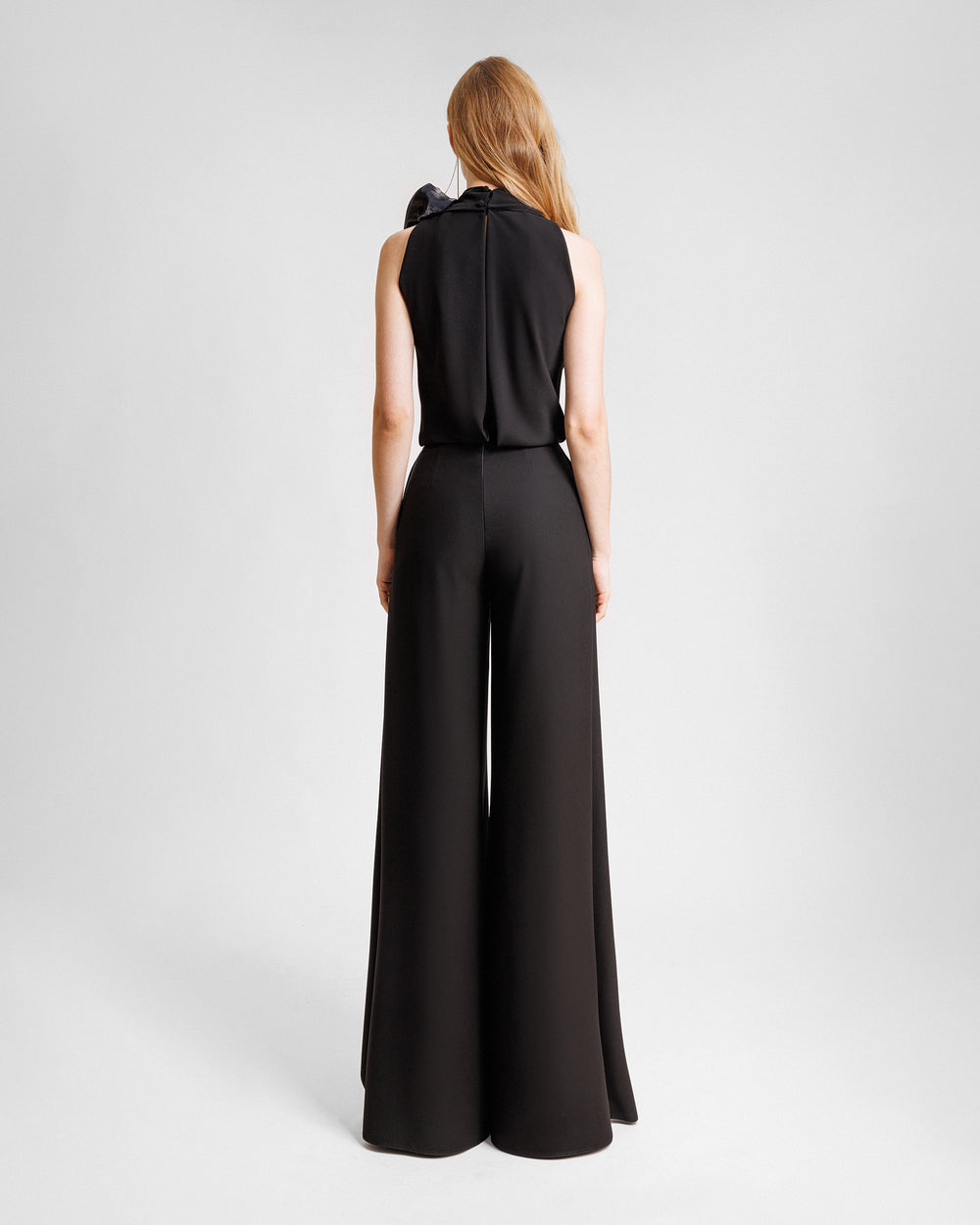 The back of an evening wear set featuring a draped loose black top with draped florals on the shoulder paired with straight-cut pants with slits on the sides.