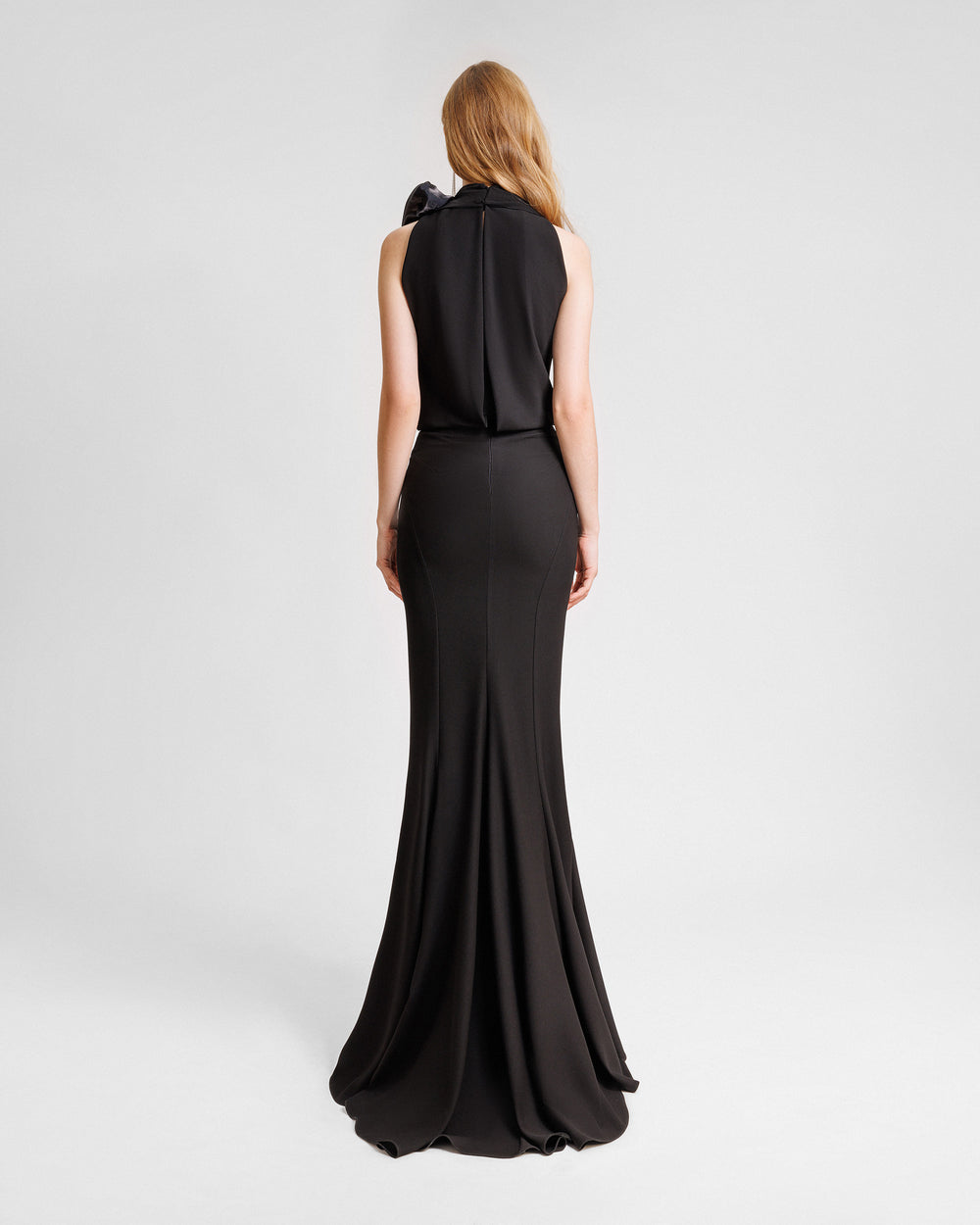 The back of a black evening wear set featuring a draped loose top with draped florals on the shoulder paired with a long slim-cut skirt.