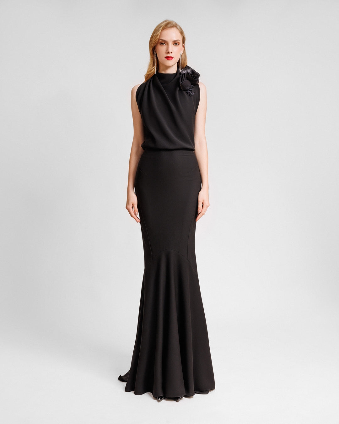 A long crepe black dress with a draped loose bodice featuring draped florals on the neckline and a straight-cut skirt. 