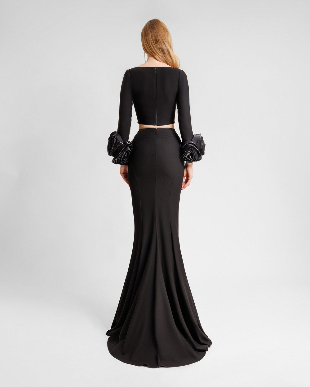 The back of a black evening wear set featuring a long sleeved crop top with floral cuffs paired with a long slim-cut skirt.