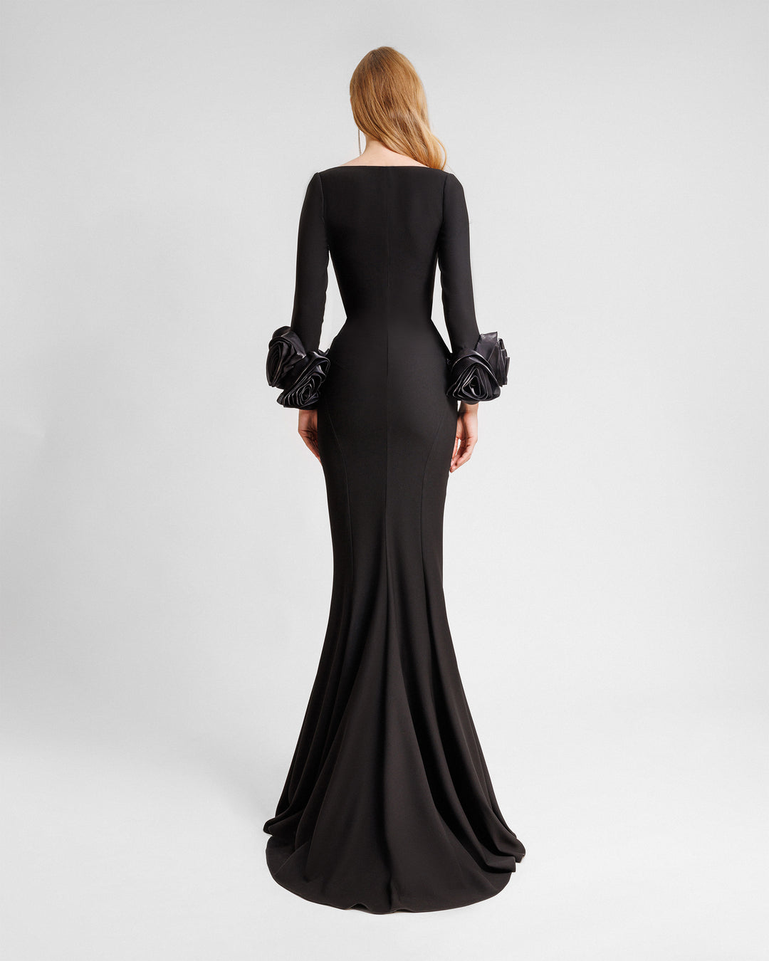 The back of a long sleeved black evening dress in crepe fabric featuring floral cuffs and a slim-cut skirt.