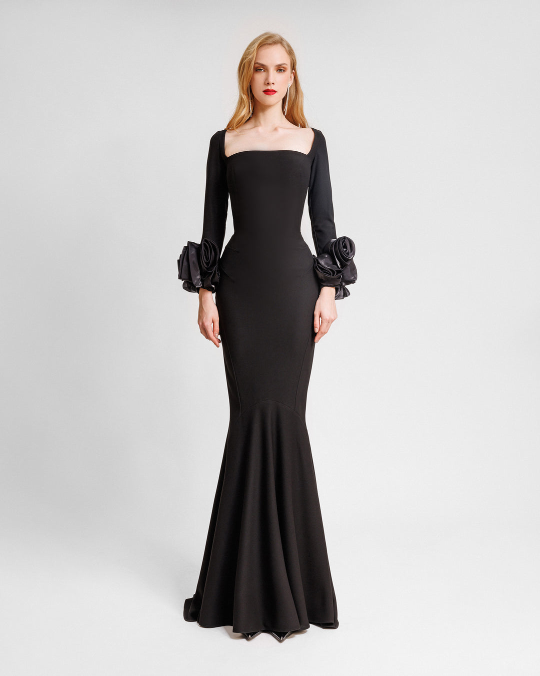 A long sleeved black evening dress in crepe fabric featuring a squared-neckline with floral cuffs and a slim-cut skirt.