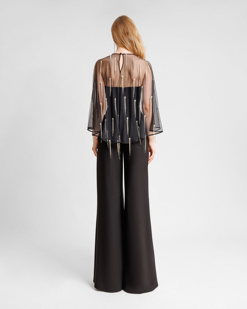 The back of a black evening wear set featuring a tube top with a beaded tulle overlay paired with straight-cut pants with slits on the sides.