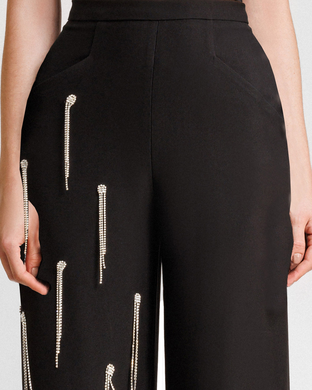 A close-up of a straight-cut black pants featuring beading fringes on a single leg.