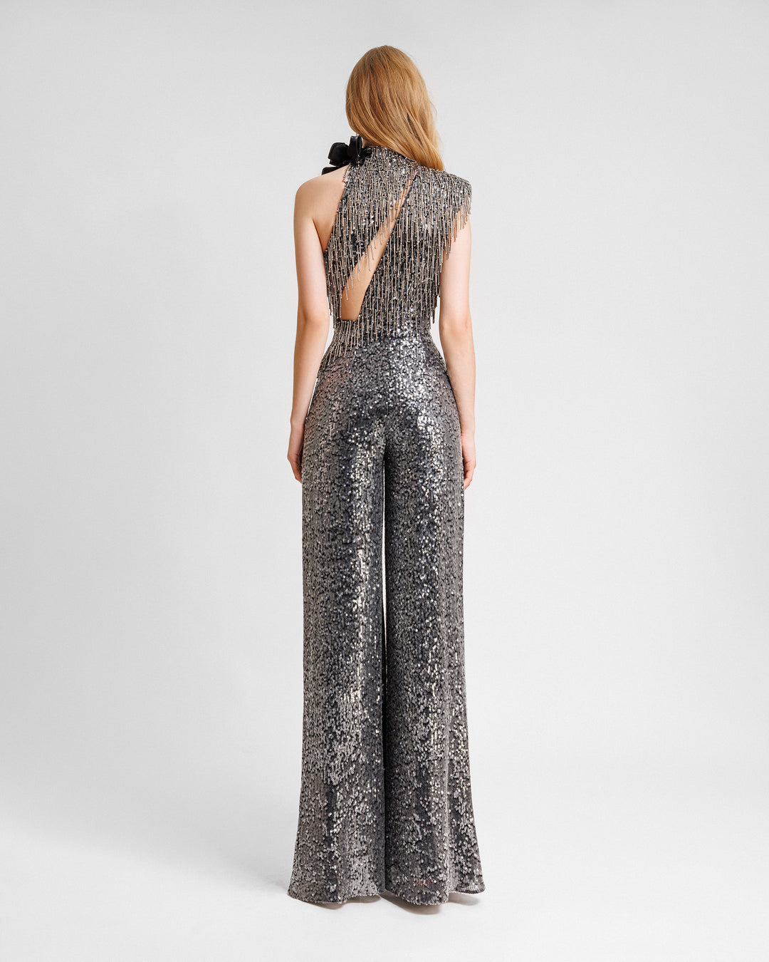 The back of an asymmetrical neckline jumpsuit with an embroidered bodice, floral draping on the shoulder, and a cut-out at the back.