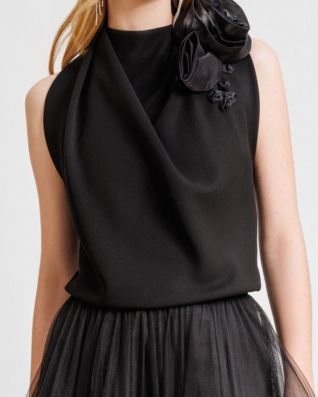 A close-up of a black evening dress featuring a loosely draped top adorned with floral draping on the shoulders.