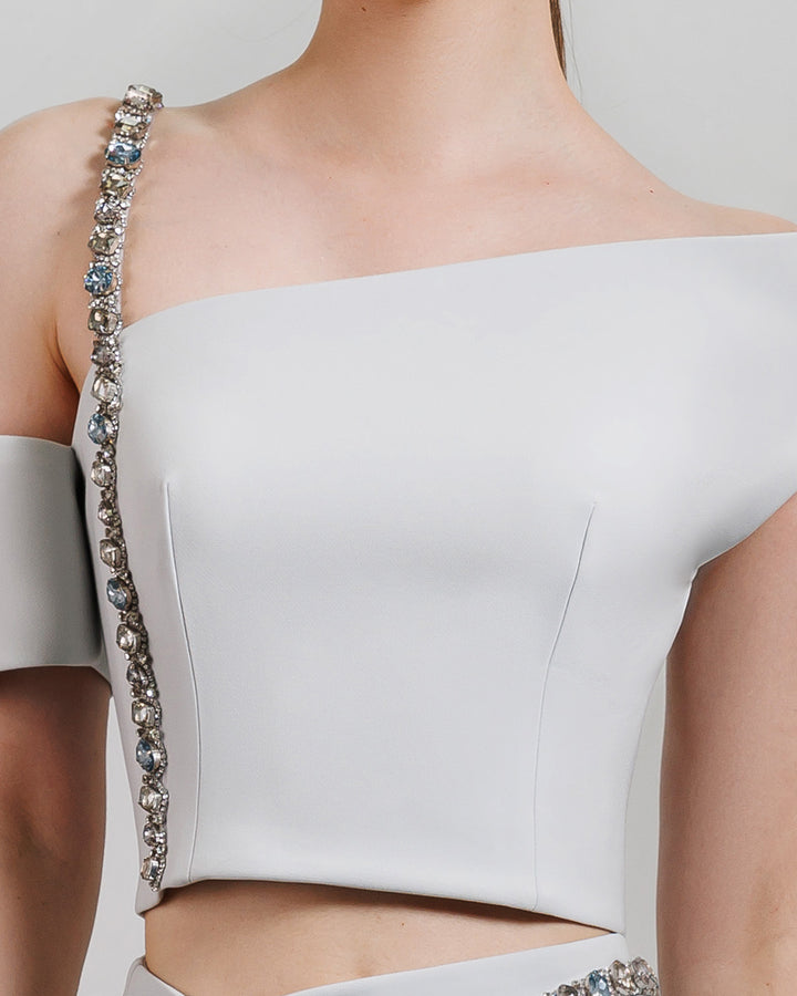 A close-up of an asymmetrical neckline top with a beaded strap.