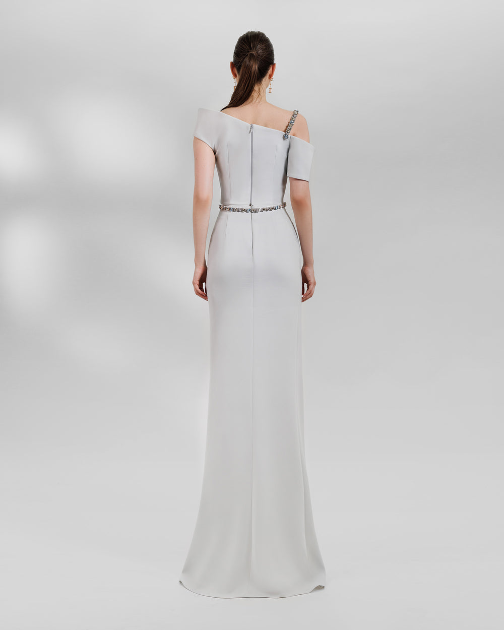 The back of an evening wear grey set featuring an asymmetrical neckline top with a beaded strap paired with a draped skirt featuring a slit on the side and a detachable belt.