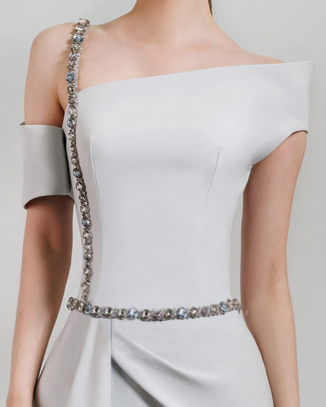 A close-up of an asymmetrical neckline grey dress with a beaded strap paired with a draped skirt featuring a slit on the side and a detachable belt.