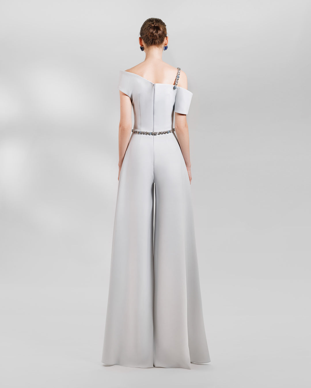 The back of an occasion outfit featuring an asymmetrical neckline grey top with a beaded strap paired a wide high waist grey pants.