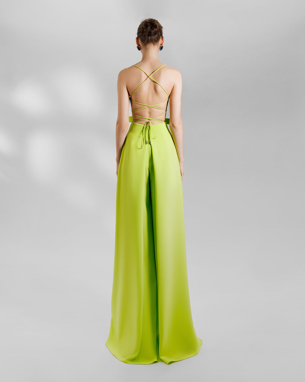 The back of a colorful look Featuring a high-waist wide pants in lime color with side pleats, and an open laced back top featuring a big sharp bow design on the waist.