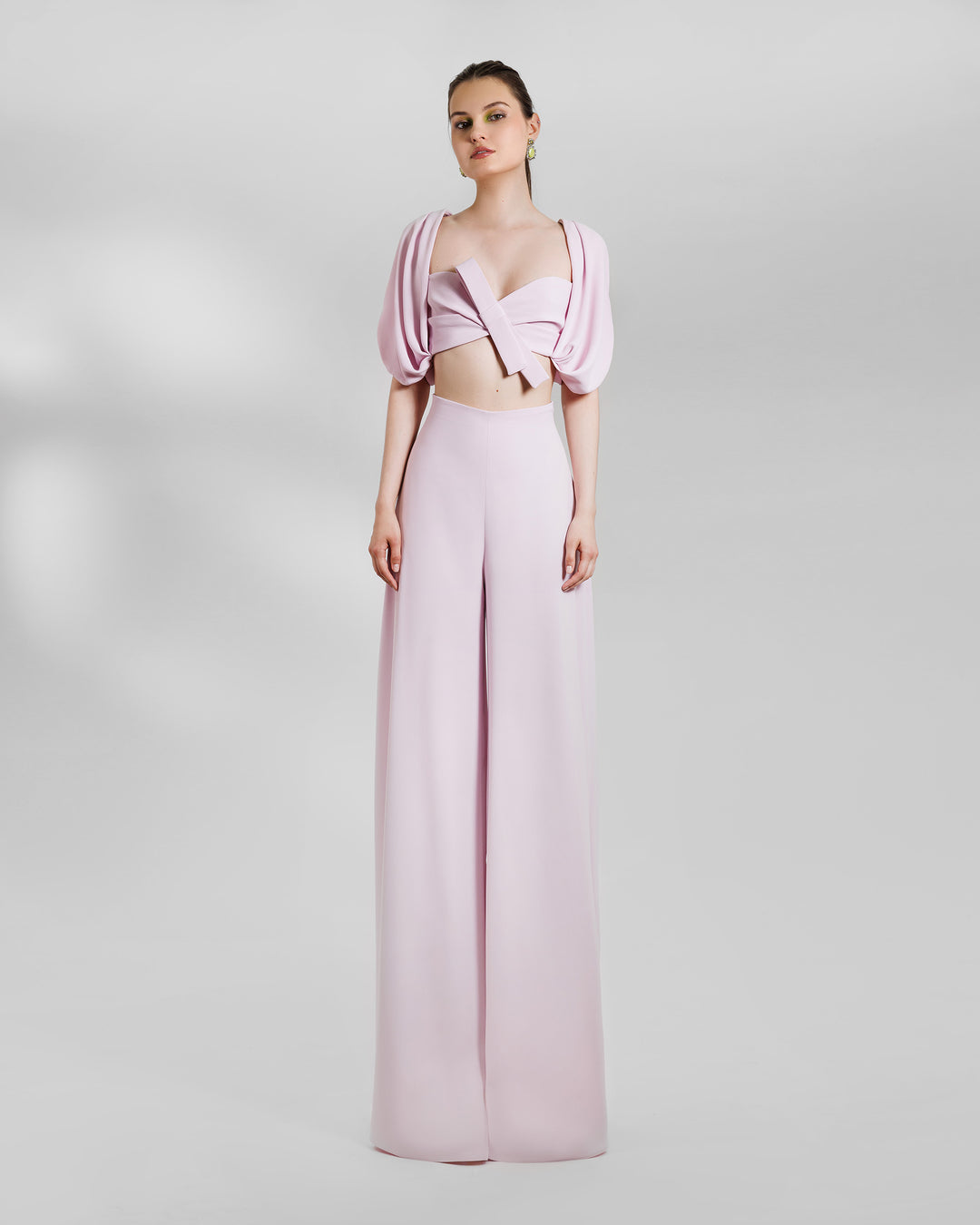 An evening wear pink set featuring a puffed-shoulders, draped cropped top paired with wide high-waist pants.