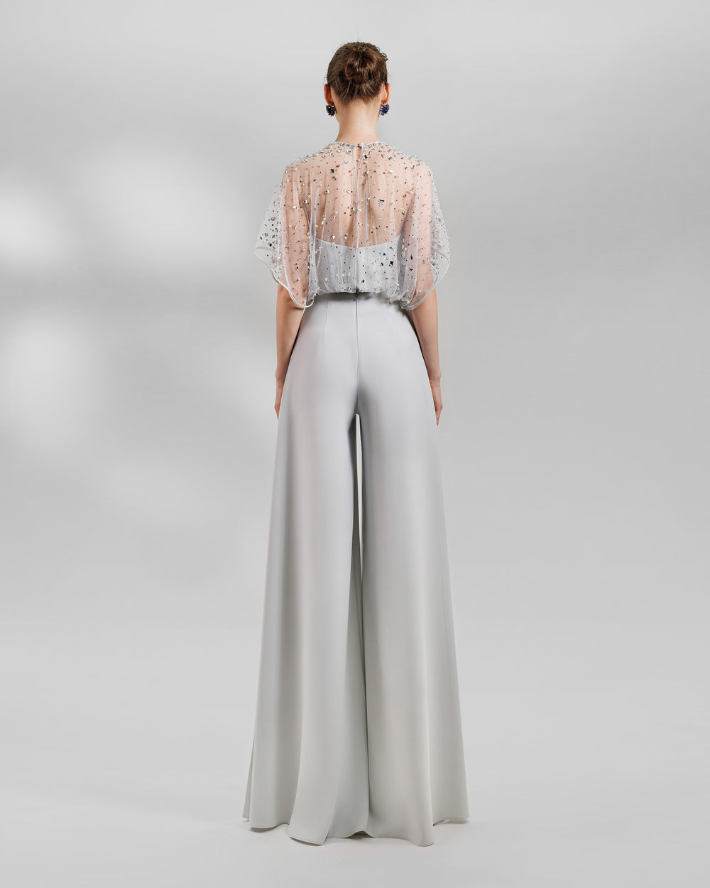 The back of an evening wear grey set featuring a fully beaded top with a crepe bow paired with a high-waist wide pants featuring open slits on the sides.