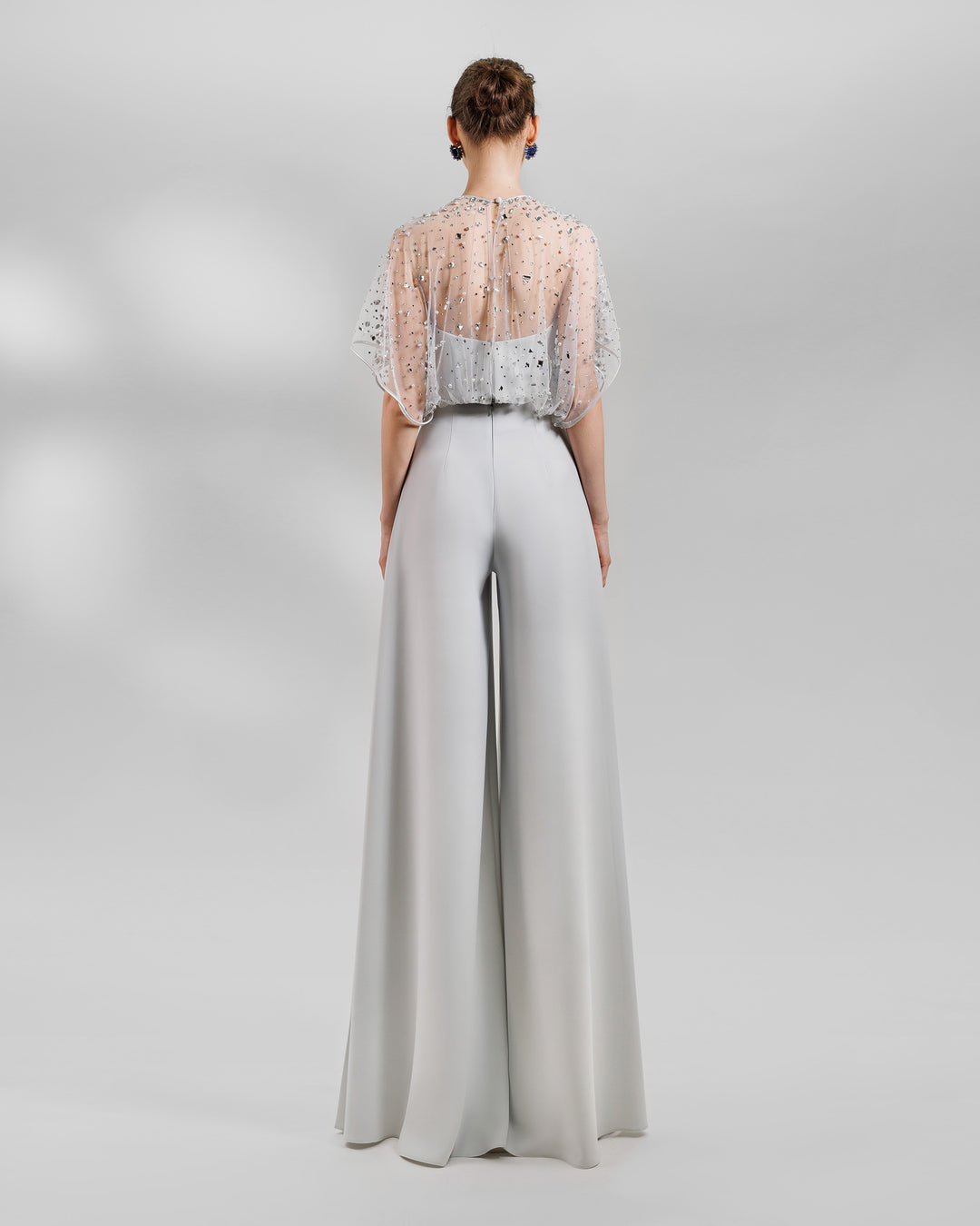 The back of an evening wear grey set featuring a fully beaded top with a crepe bow paired with a high-waist wide pants featuring open slits on the sides.