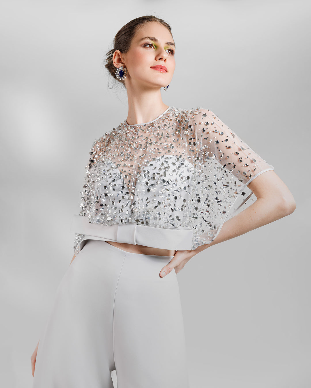 A close-up of an evening wear grey set featuring a fully beaded top with a crepe bow paired with a high-waist wide pants featuring open slits on the sides.