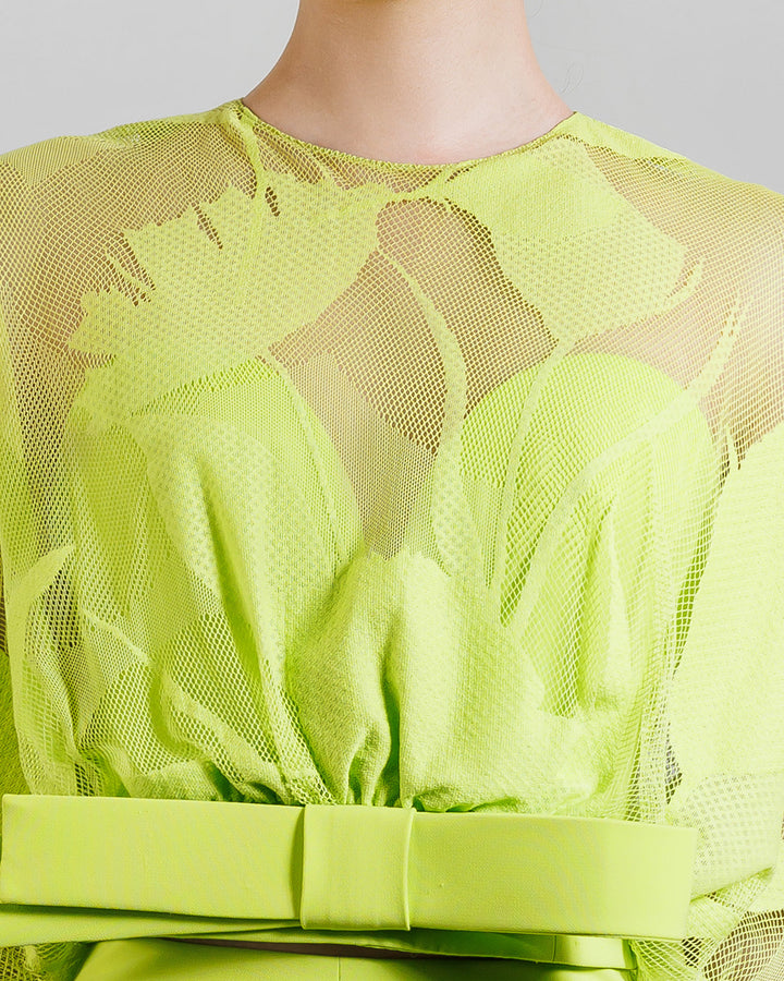 A close-up of a patterned lime lace top with a bold bow on the waist.