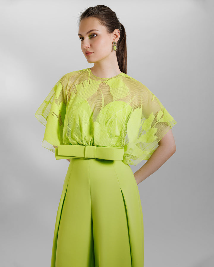 A close-up of an occasion wear featuring a patterned lace top with a bow design paired with a high-waist wide pants featuring side pleats, all in lime color.