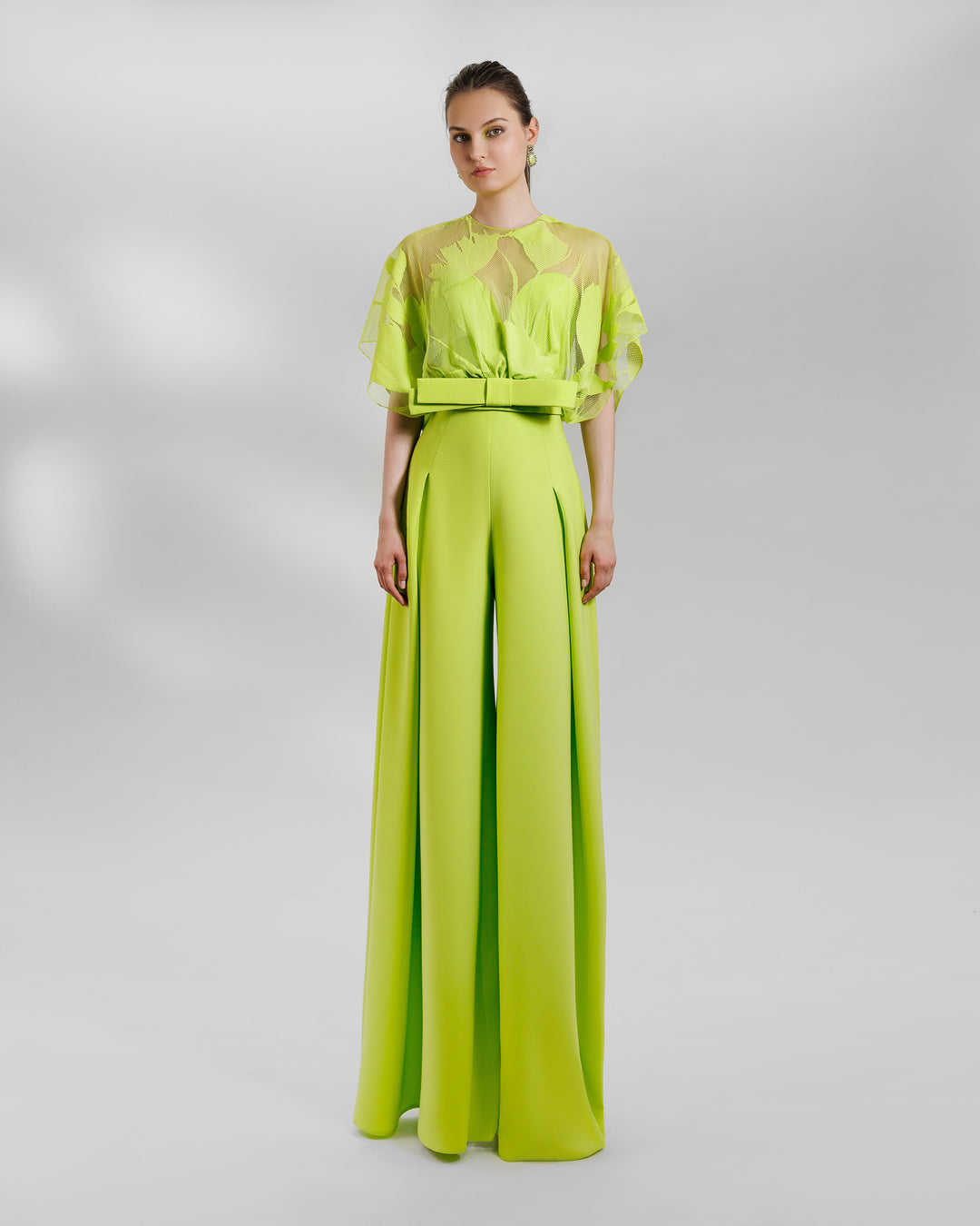 An occasion wear featuring a patterned lace top with a bow design paired with a high-waist wide pants featuring side pleats, all in lime color.