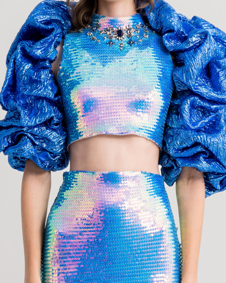 A close-up of an evening wear set featuring a beaded collar cropped-top paired with a slim pencil skirt and draped bolero all in blue color.