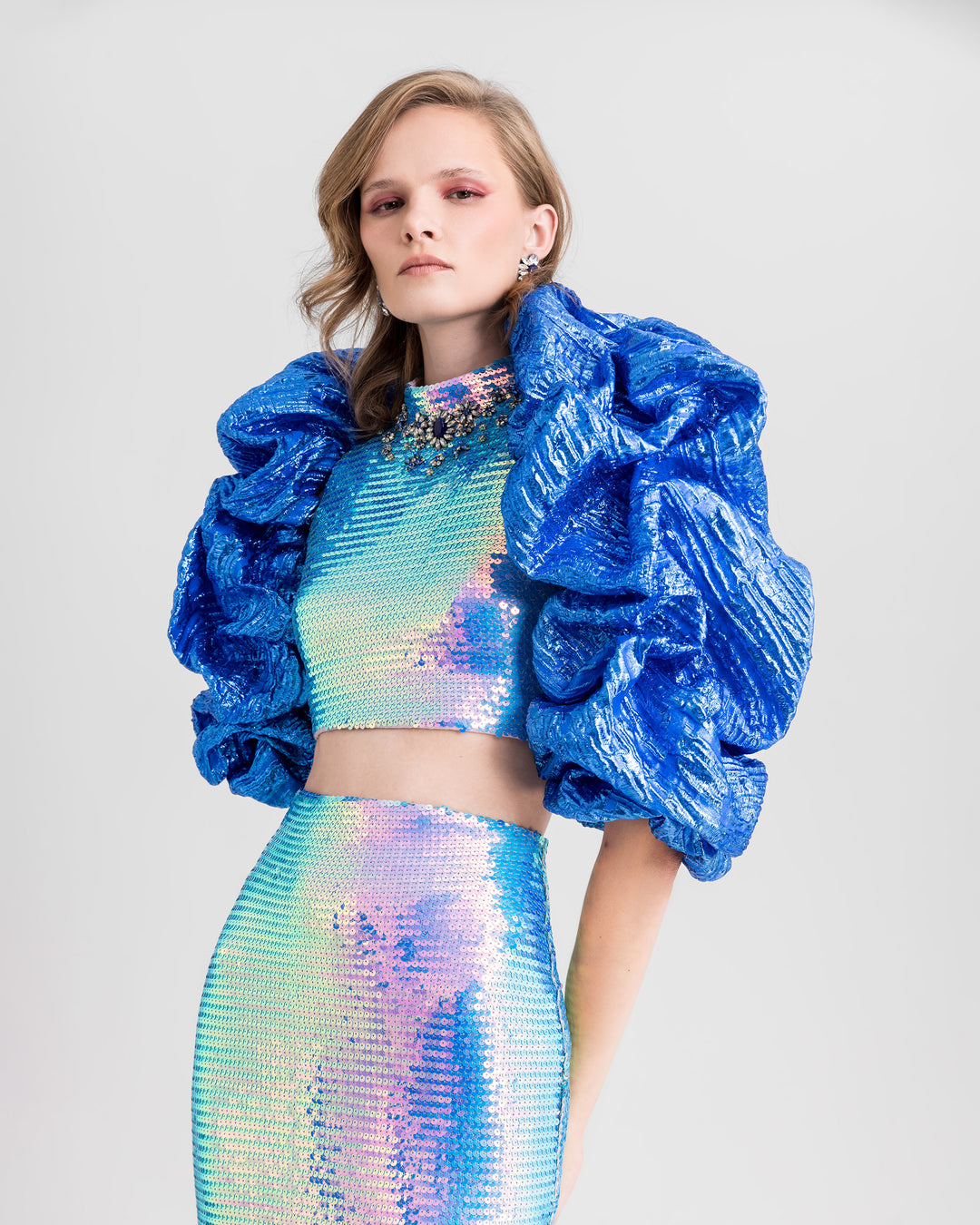 A close-up of an evening wear set featuring a beaded collar cropped-top paired with a slim pencil skirt and draped bolero all in blue color.