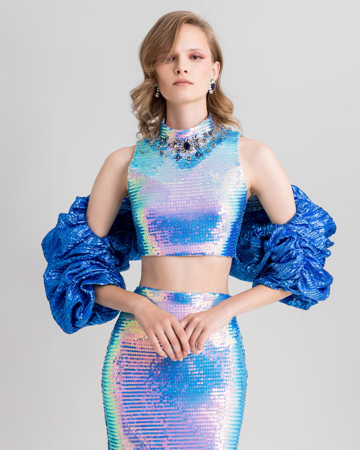 A close-up of an evening wear set featuring a beaded collar cropped-top paired with a slim pencil skirt and draped bolero all in blue color.