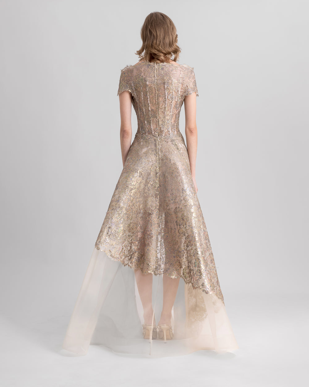 The back of an off-the-shoulders golden evening dress featuring beadings on the waist and an asymmetrical crinoline skirt.