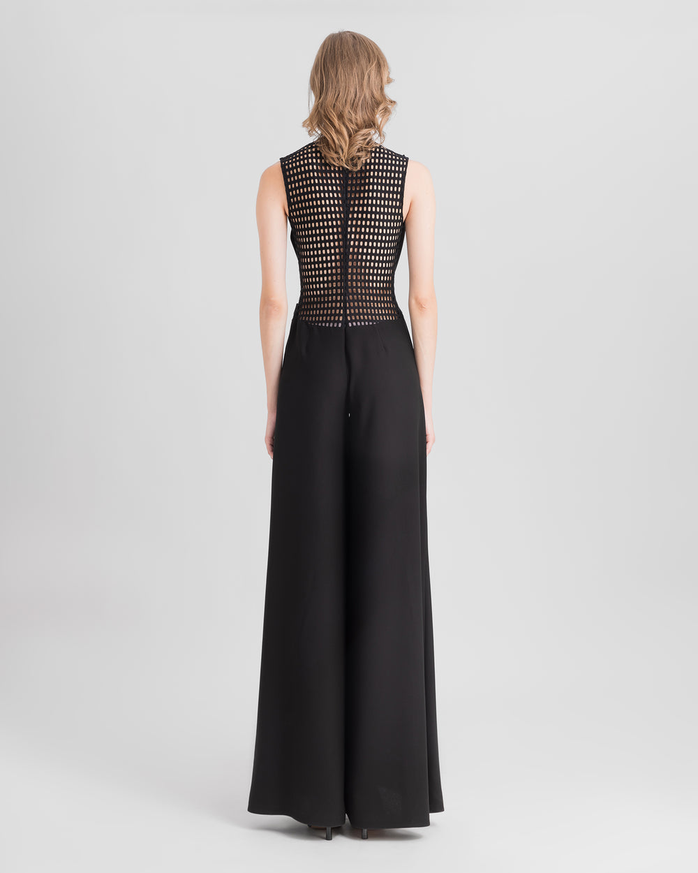 The back of a cowl-neckline black jumpsuit with crochet lace on the back, and a flared cut.