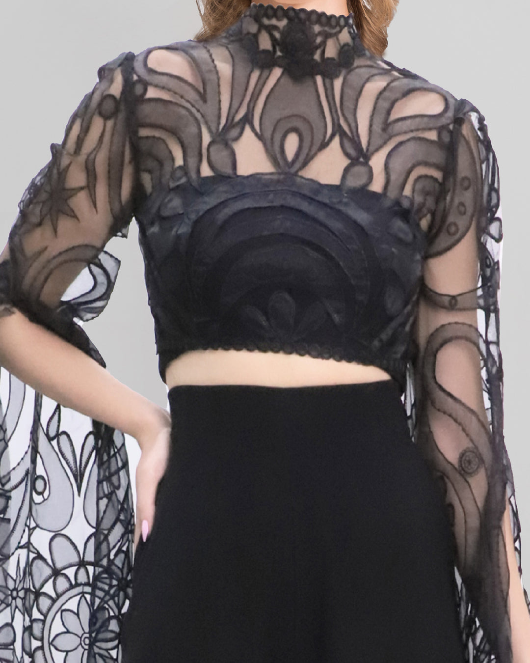 A close-up of an evening wear set featuring a black cropped lace top with floor-length sleeves, paired with a black pants featuring slits at the fronts.