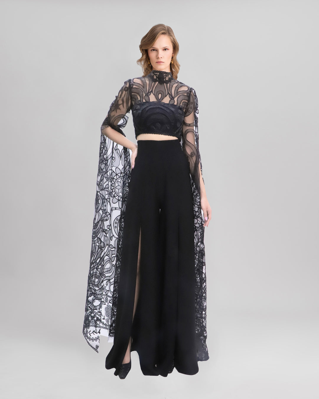 An evening wear set featuring a black cropped lace top with floor-length sleeves, paired with a black pants featuring slits at the fronts.