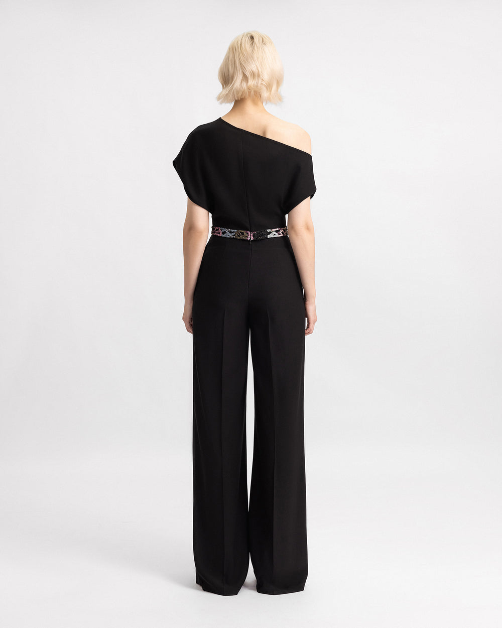 The back of a black evening wear set featuring an asymmetrical neckline top, paired with a matching beaded crepe trousers.