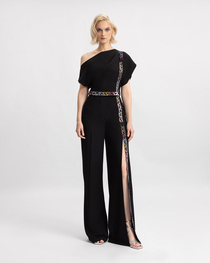 A black evening wear set featuring an asymmetrical neckline top with beading details, paired with a matching beaded trousers featuring a slit on the side.