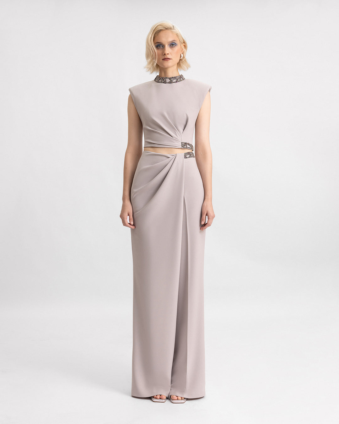 A grey evening wear set featuring a beaded high-collar top with structured shoulders paired with draped trousers.