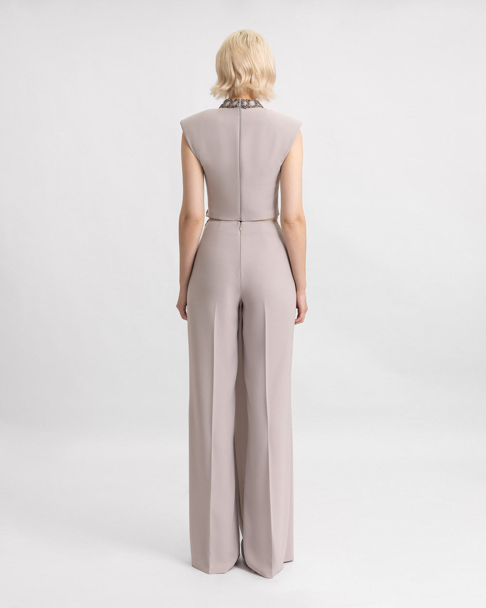 The back of a grey evening wear set featuring a beaded high-collar top with structured shoulders paired with draped trousers.