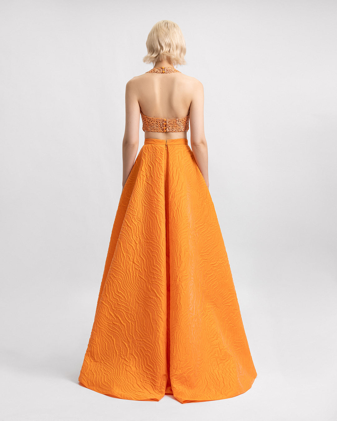 The back of an orange evening wear set featuring a halter-neckline beaded top paired with a draped long jacquard skirt.