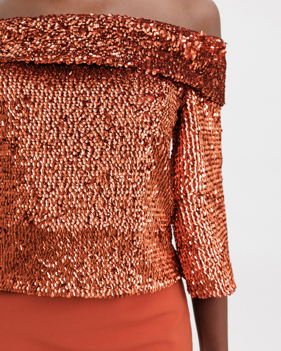 A close-up of an evening wear set featuring an off-the-shoulders copper sequins top.