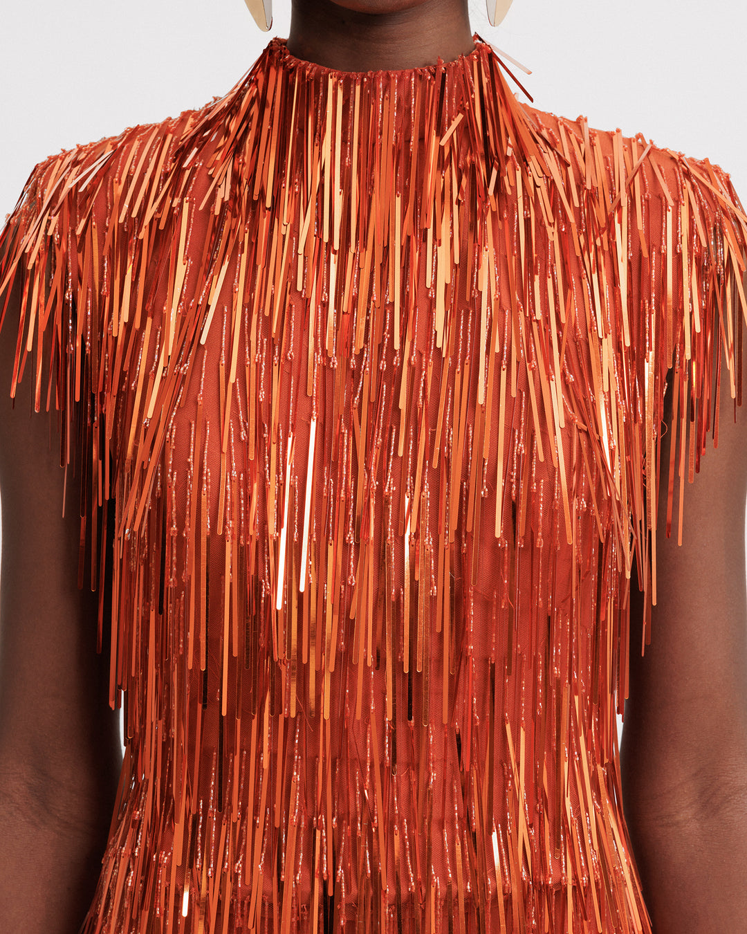 A close-up of an evening wear high-collar beaded fringes top in copper color.