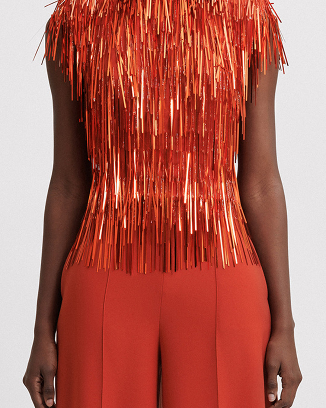 A close-up of an evening wear set featuring a high-collar beaded fringes top in copper color paired with a matching pants.