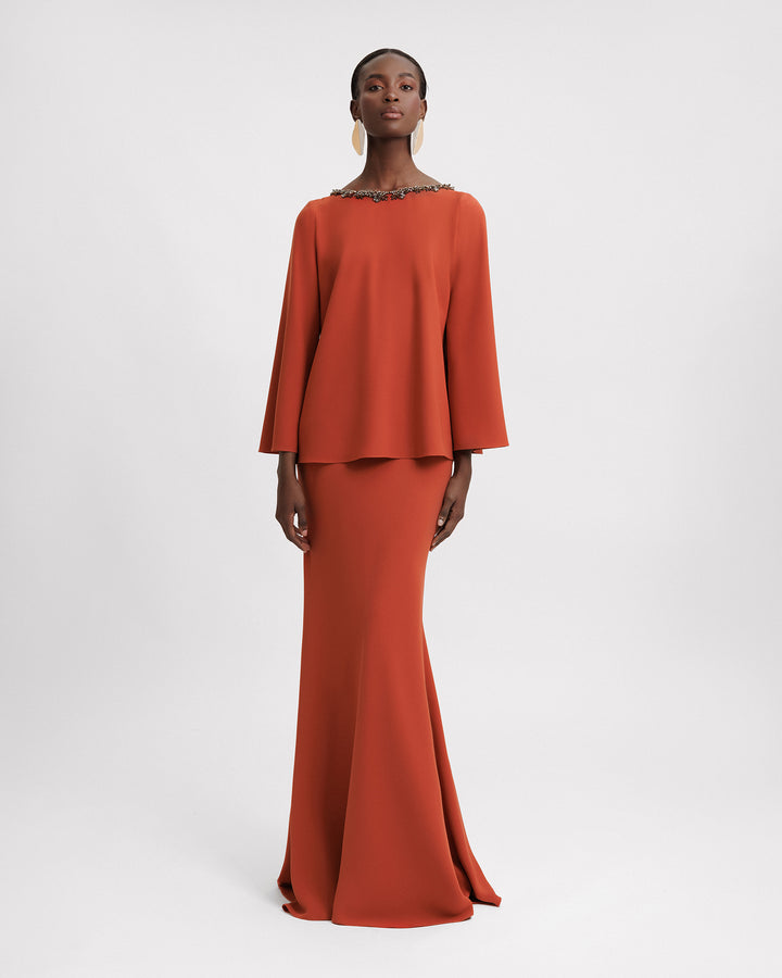 An evening wear orange set featuring a long sleeve top with a beaded neckline, paired with a slim-cut long skirt.