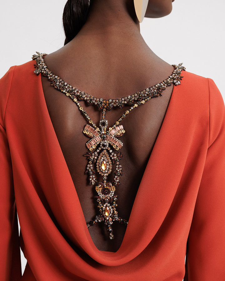 The back of an orange evening wear set featuring an cowl open back with a beaded bow design.