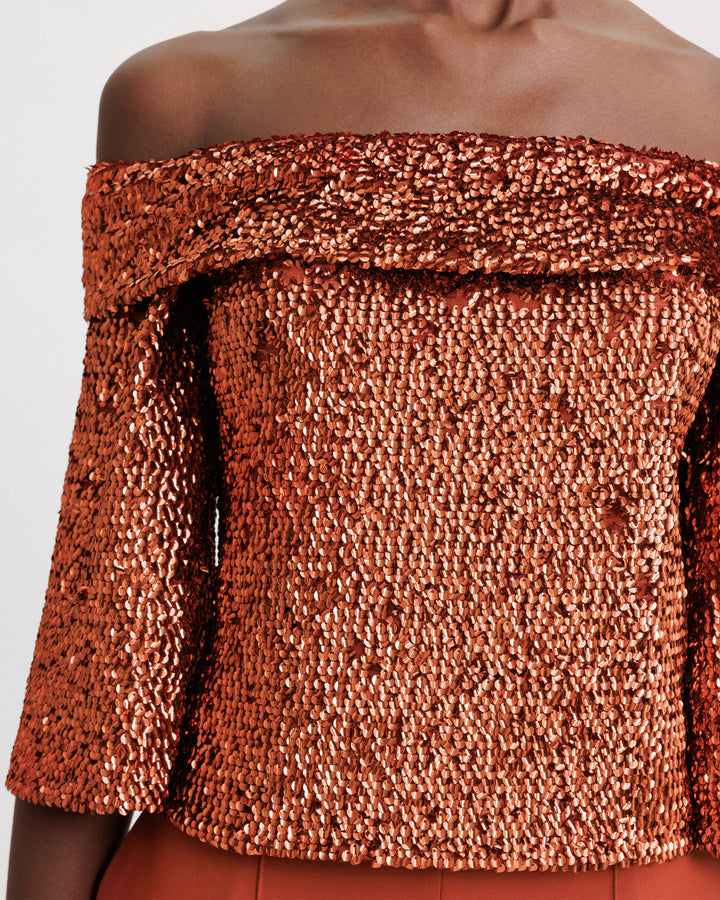 A close-up of an evening wear set featuring an off-the-shoulders copper sequins top paired with a flared pant.