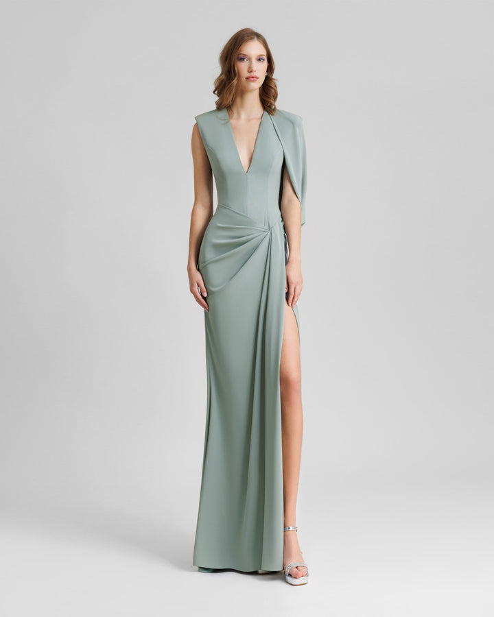 An asymmetrical teal evening dress with a bolero-like sleeve, a draped skirt and a slit on the side.