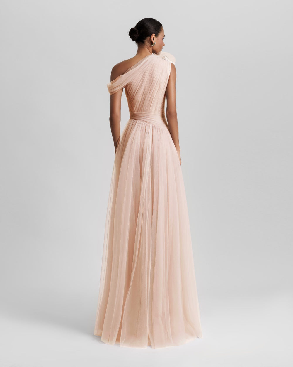 The back of an asymmetrical neckline full tulle long dress in blush color, with ruffled side slit and draping design on the bodice.