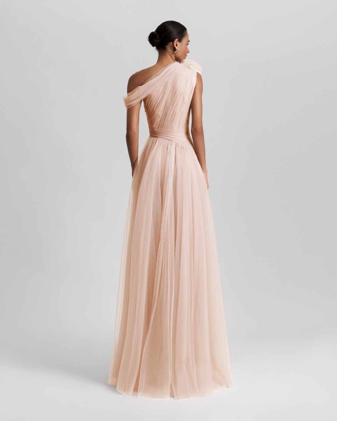 The back of an asymmetrical neckline full tulle long dress in blush color, with ruffled side slit and draping design on the bodice.